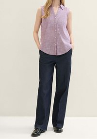 Blusa sin mangas de cuadros lilas claros con cuello en punta, acompañada de pantalones de pierna ancha de color azul oscuro y zapatos negros.