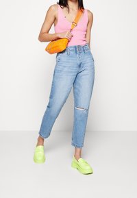 Vaaleanpunainen ribbattua tankkia, korkeavyötäröiset siniset farkut, joissa on revityt polvet, kirkkaan oranssi tikkikangasta käsilaukku ja neonvihreät platform-kengät.