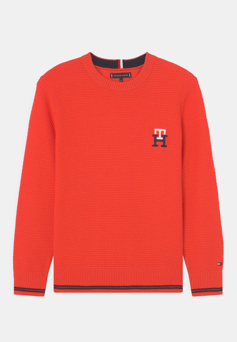 Pull en tricot rouge avec col rond, motif texturé, petits logos Tommy Hilfiger sur la poitrine et le poignet, et détails en rayures navy sur les poignets et l'ourlet.