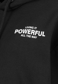 Schwarzer Kapuzenpullover aus Baumwolle mit glatter Textur. Mit weißem Drucktext: "LIVING IT POWERFUL ALL THE WAY."