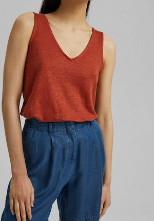 Roestkleurige tanktop met een V-hals, gemaakt van een textuurrijke stof. Gecombineerd met losse blauwe denim shorts met plooien.