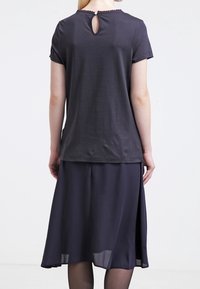 Tmavě šedé tričko s krátkým rukávem a malým otvorem na zádech, spárované s volnou tmavě šedou sukní, která má průsvitný lem.