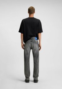 Black oversized t-shirt with short sleeves, paired with gray straight-leg jeans. Notable blue logo patch on the waistband. Simple, textured design.
