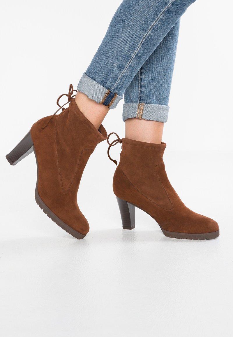 Bottines en daim marron à talon haut, avec un bout arrondi, des coutures latérales courbées et des lacets à l'arrière. Semelle en caoutchouc pour une meilleure adhérence.