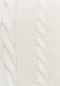 Valkoinen neulottu neulepaita, joka esittelee kaapelitekstiilimallia, paksua rakennetta ja vaihtelevia ribbireunuksia visuaalisen mielenkiinnon lisäämiseksi.