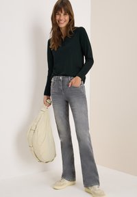 Polo shirt noir à manches longues, jeans grisonnants évasés et baskets beiges. Tenant un sac rond rembourré de couleur beige clair. Design simple et décontracté.