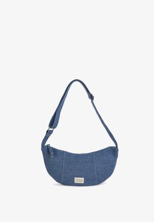 Blue denim shoulder bag with a curved shape, single shoulder strap, and a silver brand tag. Soft texture with visible seams and stitches.