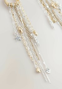 Zlate in srebrne verige z različnimi obeski, vključno z zvezdami in listi, ki se ponašajo z lesketajočimi teksturami in raznolikimi dolžinami.