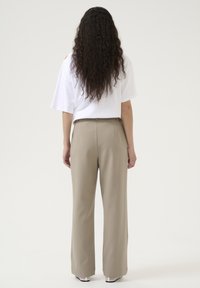 Beige vida byxor med texturerad yta, med midjeband, bältesöglor och en matchande lös vit kortärmad topp.