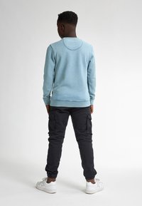Felpa azzurra chiara con scollatura a girocollo, pantaloni cargo neri con tasche laterali e sneaker bianche. Texture liscia, vestibilità casual.