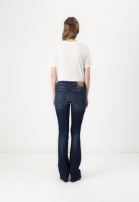Dunkelblaue Schlagjeans aus Denim mit mittelhohem Bund und zwei Gesäßtaschen. Getragen mit einem schlichten weißen T-Shirt.