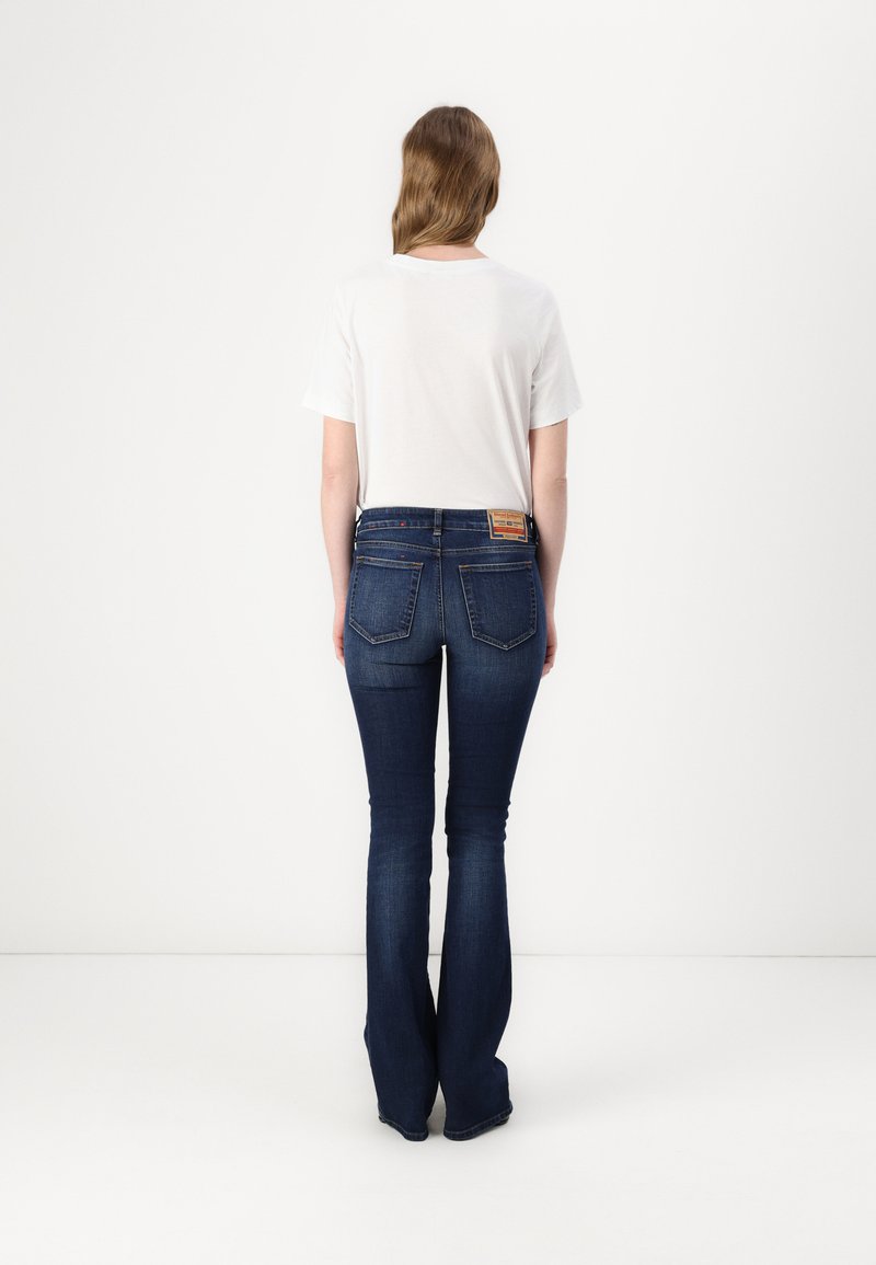 Dunkelblaue Schlagjeans aus Denim mit mittelhohem Bund und zwei Gesäßtaschen. Getragen mit einem schlichten weißen T-Shirt.