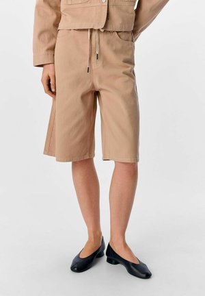 Beiga bomullsshorts med elastisk midja och dragsko. Har en något lös passform som slutar strax ovanför knäet. I kombination med svarta lågklackade skor.