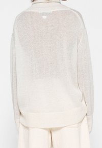 Maglione oversize beige chiaro con una finitura testurizzata, caratterizzato da un ampio orlo a coste e una leggera lucentezza, mostrato da dietro.