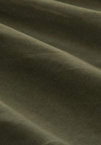 Olive zöld pamut anyag, lágy textúrával, finom bordázott mintákkal és gyengéd redőkbe hajtva, sima, leplezett megjelenést kölcsönözve.