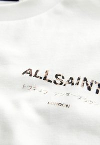 Bílá bavlněná tričko s textem "ALLSAINTS" ve vzorovaném designu, s dalším textem v japonštině a "LONDON" tištěným menším písmem.