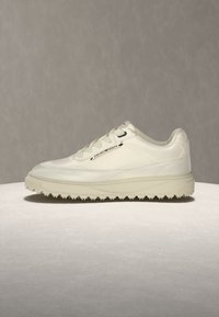 Λευκό sneaker χαμηλού προφίλ με υφή στη σόλα, σχεδιασμό με κορδόνια και ετικέτα "Emporio Armani" στο πλάι σε απλό φόντο.