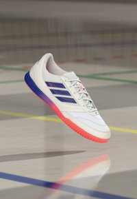 White athletic shoe with mesh and synthetic upper, featuring three navy stripes, pink accents, and a gradient rubber sole transitioning from pink to blue.