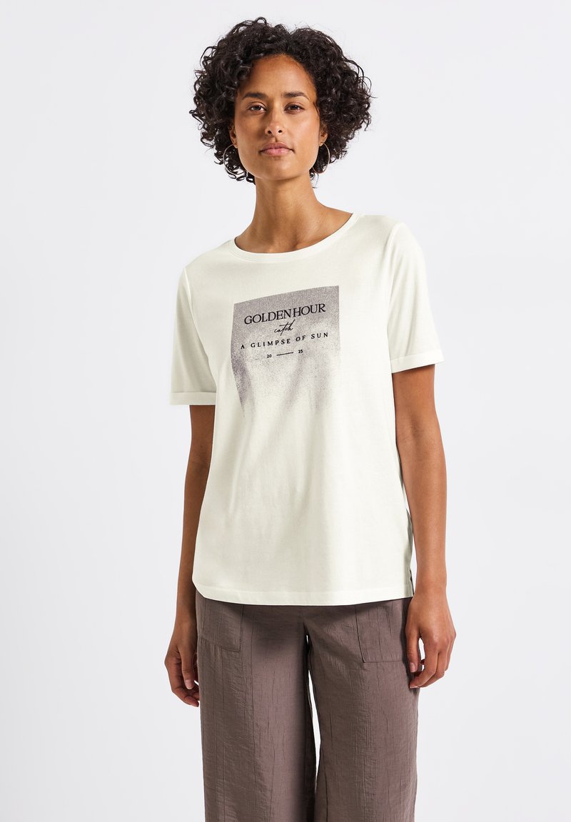 T-shirt crème clair avec un col rond et des manches courtes, arborant un imprimé graphique gris avec la mention "GOLDENHOUR UN APERÇU DU SOLEIL."