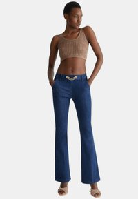 Jeans a gamba larga blu scuro con una texture liscia e un dettaglio della cintura in catena dorata decorativa, abbinati a un top corto marrone dalla texture lavorata.