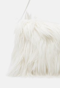 Biały sztuczny futrzany worek o miękkiej, puszystej fakturze, z prostym wzorem i płaskim kształtem. Góra ma gładki biały pasek do noszenia.