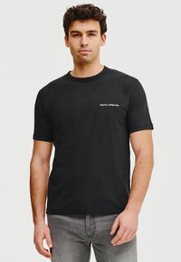 Czarna bawełniana koszulka z okrągłym dekoltem i krótkimi rękawami, z małym białym logo na lewej stronie klatki piersiowej.