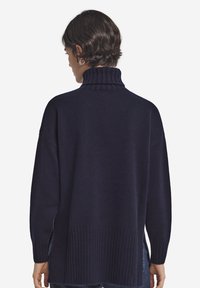 Marinblå tröja med hög ribbad krage, oversize passform, sidospjäll och stickad textur. Inga synliga mönster eller metallbeslag.