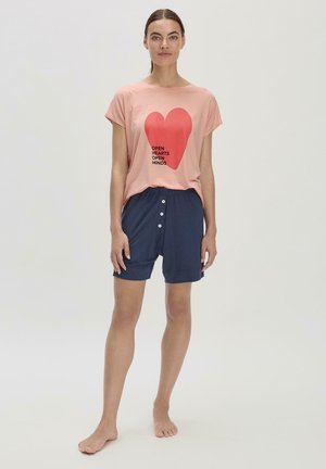 Helles rosa T-Shirt mit einem roten Herzensgrafik und Text, kombiniert mit navyblauen Shorts mit vorderen Knöpfen und einer lockeren Passform.