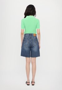 Mint green polo shirt with white collar, paired with blue denim shorts that have a loose fit and visible back pockets.