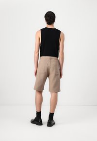 Beige gestreifte Shorts aus Baumwolle mit einer Gesäßtasche, kombiniert mit einem schwarzen ärmellosen Shirt und schwarzen Socken mit Schuhen.