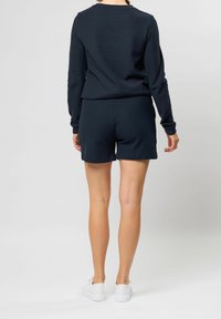 Granatowa bluza z długim rękawem i dopasowane szorty, wykonane z materiału o fakturze. Białe sneakersy dopełniają strój. Skupienie na prostym, codziennym designie.