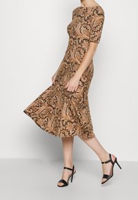 Brun klänning med paisley-mönster, kortärmad och med utsvängd kjol. Matchas med svarta klacksandaler med remmar.