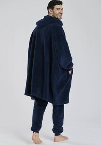 Marineblå, blødt stof poncho med hætte, med brede ærmer og forlommer, parret med matchende tætsiddende bukser. Blød tekstur.