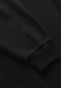 Tessuto di felpa nera con polsini a coste, texture liscia e design semplice. Nessun logo o motivo visibile. Vista ravvicinata.