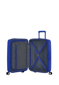 Valigia rigida blu con scomparti interni, dotata di tasca con zip e cinture elastiche incrociate, montata su quattro ruote per facilitare la mobilità.