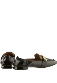 Mocassins en cuir verni noir avec un talon plat, un bout pointu et un accent en métal doré à l'avant. Texture lisse avec un design élégant.