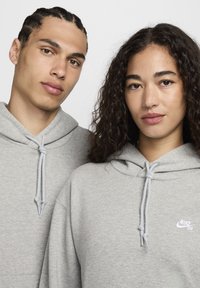 Grå hettegensere laget av en bomullsblandingsstoff, med snorer og en liten hvit Nike SB-logo på brystet.
