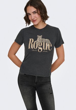 Junge Frau trägt ein ausgewaschenes schwarzes T-Shirt mit einem Leopardenmotiv und dem Schriftzug "Rogue", kombiniert mit dunklen, leicht ausgewaschenen Jeans.