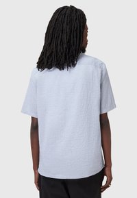 Camicia azzurro chiaro a maniche corte con tessuto testurizzato, taglio dritto e vestibilità comoda. Presenta un orlo arrotondato e un dettaglio sulla spalla posteriore.