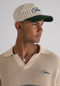 Casquette rayée beige et verte avec une visière incurvée, ornée de broderies bleu marine à l'avant et d'une texture de tissu lisse.