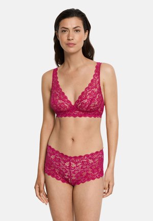 Donna in piedi che indossa un reggiseno e slip boyshort in pizzo floreale magenta coordinati, su uno sfondo chiaro e semplice.