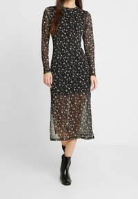 Svart blommig klänning med långa genomskinliga ärmar och midilängd. Har ett utsökt blommönster; bärs med ankelskor.