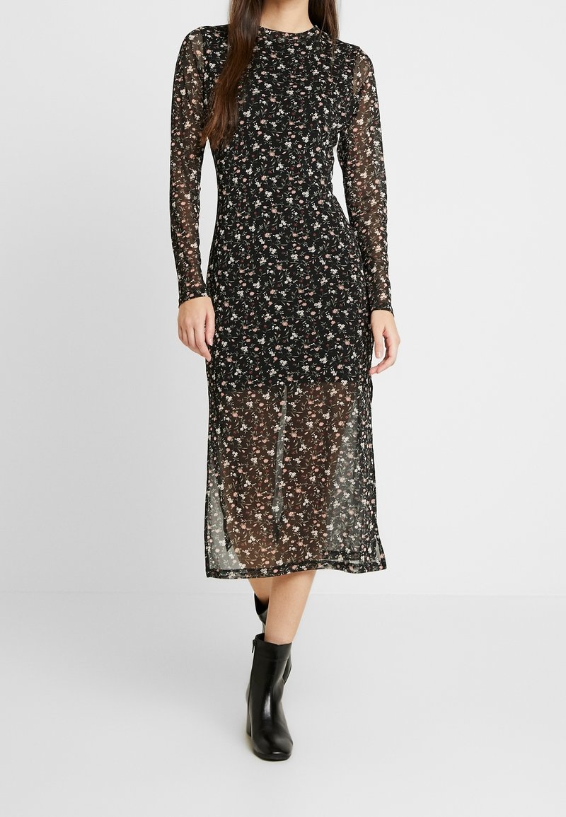 Svart blommig klänning med långa genomskinliga ärmar och midilängd. Har ett utsökt blommönster; bärs med ankelskor.