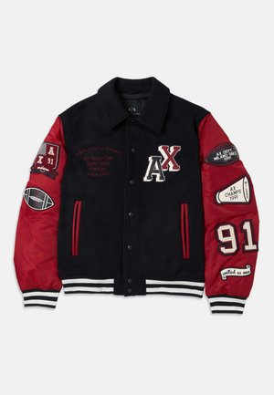 Juodas vilnos ir raudono nailono varsity švarkas su siuvinėtais ženklais, dryžuotais rankogaliais, snap mygtukais ir numeriu „91“ ant rankovės.