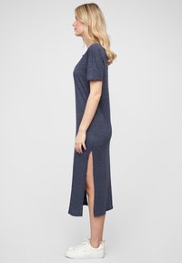 Tengerészkék, térdig érő pólóruha rövid ujjakkal, oldalsó hasítékokkal, puha kötött anyagból. Fehér sportcipővel párosítva.