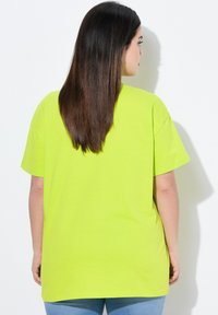 Jasně neonově žluté oversized tričko s krátkým rukávem a kulatým výstřihem, vyrobené z měkké bavlněné látky. Pohled zezadu ukazuje hladkou texturu.