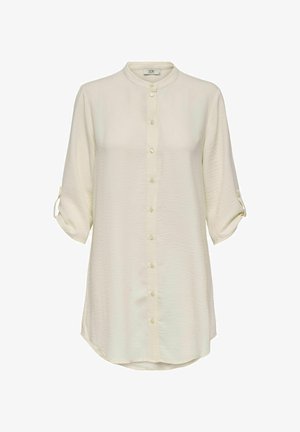 Light beige long-sleeve shirt with a mandarin collar, front buttons, and rolled cuffs. Made of soft, textured fabric with a rounded hem.