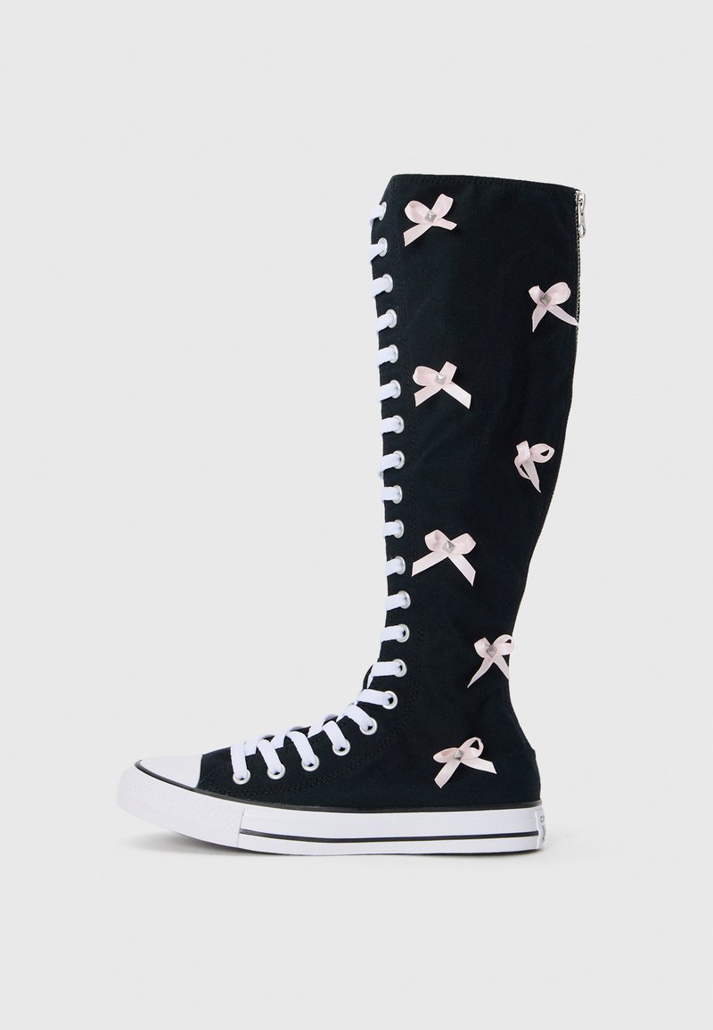 Must ehk põlvekõrgused mustad kanged saapad valgete paeltega, mille külgedel on roosad satiinist lipsud ja külgmine tõmblukk. Tugev kummist tallaga hallide aktsentidega.