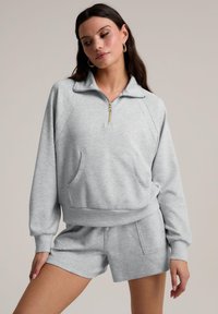Sweat-shirt zippé gris avec col, poignets côtelés et poche avant, associé à un short assorti. Tissu doux avec une texture subtile.