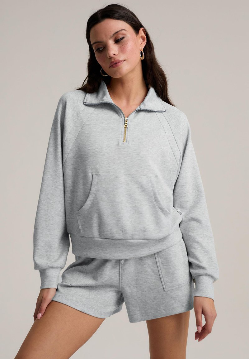 Sweat-shirt zippé gris avec col, poignets côtelés et poche avant, associé à un short assorti. Tissu doux avec une texture subtile.